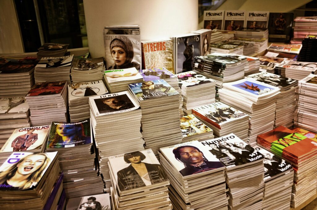 Huge stacks of diverse fashion and lifestyle magazines piled high in an indoor store setting.