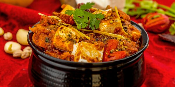 Spicy paneer tikka masala garnished with cilantro and spices on a vibrant red background.