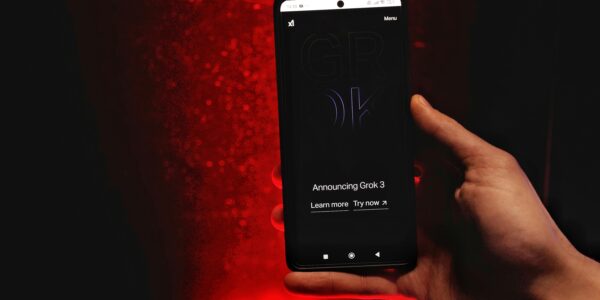 A hand holds a smartphone displaying Grok 3 announcement against a red background.