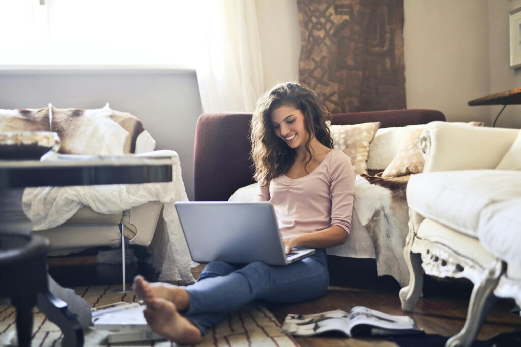 How to Effectively Manage Time While Working from Home - 2025 2 Smiling woman using a laptop seated on the floor in a cozy living room, working remotely.