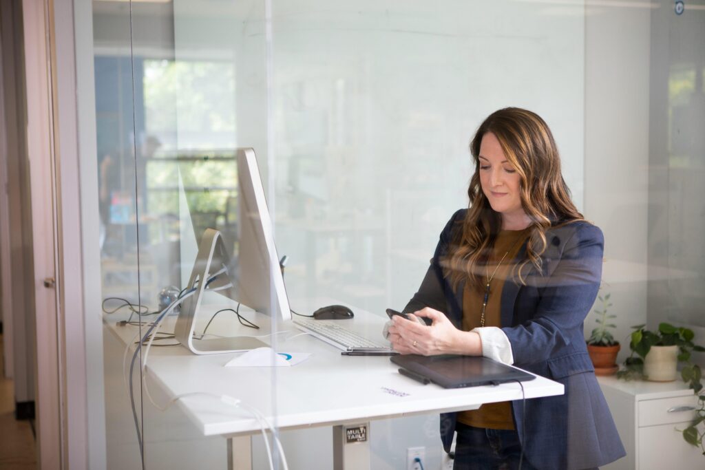 What Are the Benefits of Using a Standing Desk? 2 Businesswoman in a blazer using her smartphone at a standing desk in a modern office.