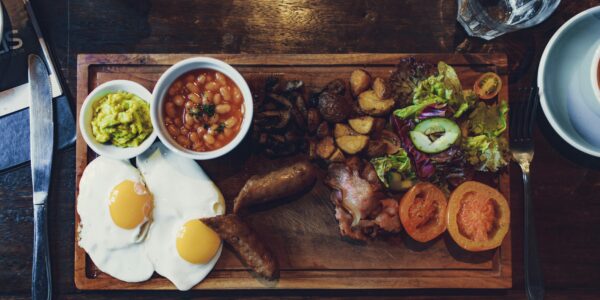 Top view of delicious fried eggs and vegetables with sausages and beans on wooden tray with fork and knife