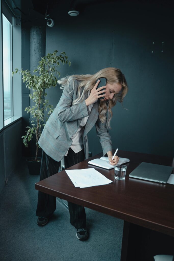 What Are the Benefits of Using a Standing Desk? 5 A businesswoman multitasks by talking on the phone while taking notes at her office desk.