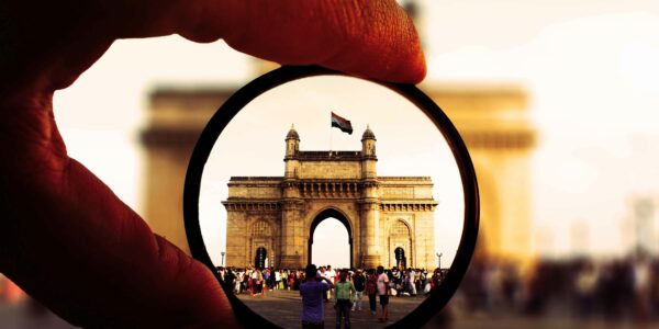 Artistic view of the Gateway of India through a camera lens filter with vibrant colors and bustling crowd.