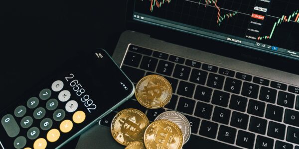 A still life of Bitcoin coins, a smartphone calculator, and a trading chart on a laptop.