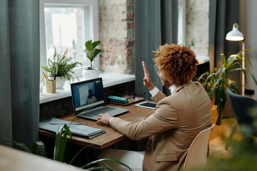 Business professional waving during a video call in a stylish modern office setting.