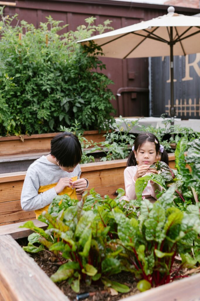 What Are the Steps to Start a Community Garden 4 Two children observing plants in a lush outdoor garden, immersed in nature exploration.